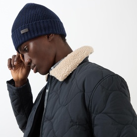 Model wearing Barbour Carlton navy wool beanie hat with ribbed structure and logo tab, styled with a quilted jacket with sherpa collar