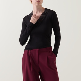 Model wearing Masai Dionius Lace Trim Top in black with lace V-neckline and long sleeves, styled with dark red wide-leg trousers