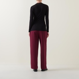 Model wearing Masai Dionius Lace Trim Top in black with long sleeves, styled with wide-leg burgundy trousers