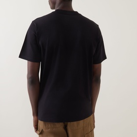 Model wearing Carhartt Script Logo T-Shirt in black, rear view, crew neck, short sleeves, straight hem, styled with tan cargo trousers.