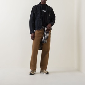 Model wearing Carhartt Script Logo T-Shirt in Black/White with dark overshirt, tan trousers, and plaid shirt tied at waist.
