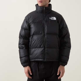 Model wearing North Face black nylon puffer jacket with high collar, chest logo, and quilted panels, styled with black trousers.