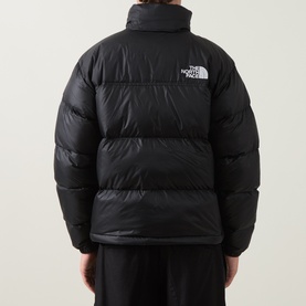 Model wearing The North Face black nylon puffer jacket, rear view, showing quilted panels and logo patch on chest.