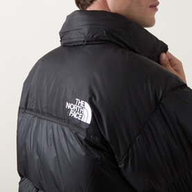 Model wearing North Face black nylon casual jacket, close-up of back showing logo patch and quilted puffer detailing.