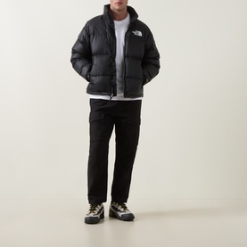 Model wearing North Face black nylon puffer jacket with white logo, styled with white tee, black trousers and trail trainers.