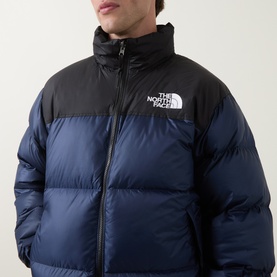 Model wearing North Face 1996 Retro Nuptse Down Jacket in navy and black, showing quilted panels, stand collar, and logo chest print