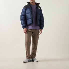 Model wearing North Face 1996 Retro Nuptse Down Jacket in navy/black, styled with lilac hoodie, tan cargo trousers and grey trainers
