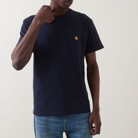 Model wearing Carhartt Chase Logo T-Shirt in navy, crew neck with gold embroidered chest logo, styled with blue jeans.