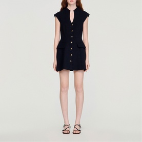 Model wearing Sandro Button Front Mini Knitted Dress in black, sleeveless with V-neckline, front buttons and flap pockets, styled with strappy sandals