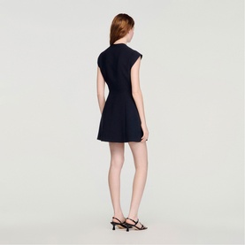Model wearing Sandro Button Front Mini Knitted Dress in black, sleeveless with voluminous skirt. Styled with black strappy heeled sandals.
