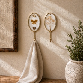 Mindy Browne Floral Butterfly Two-Piece Wall Hook Set in gold, oval glass frames with butterfly and floral motifs, one holding a cream towel