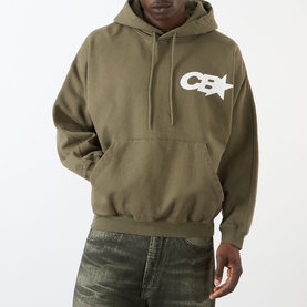 Model wearing Cole Buxton Star Racing Hoodie in khaki with white CB star logo on chest, paired with distressed jeans.