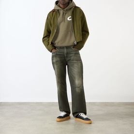 Model wearing Cole Buxton Star Racing Hoodie in khaki with contrast chest logo, styled with olive jeans and black low-top trainers.