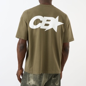 Model wearing Cole Buxton khaki cotton T-shirt, back view showing large white CB star graphic print, styled with distressed jeans