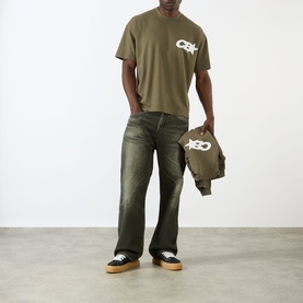Model wearing Cole Buxton khaki cotton T-shirt with logo print, styled with dark wash jeans and trainers. Model carrying matching khaki bag.