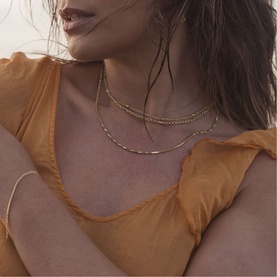 Model with Juvi Koh Tao Chain Necklace in gold, alternating open chain links, layered with a second necklace. Styled with a gold bracelet