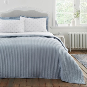 Bianca Quilted Lines Bedspread Blue, with channel-stitched texture, draped over a double bed with white star-print pillowcases