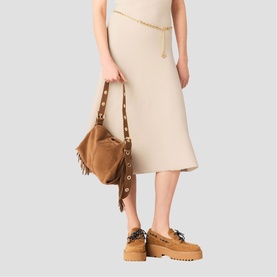 Model carrying Maje beige suede shoulder bag with gold eyelet trim and fringe detail, styled with cream midi dress and tan loafers