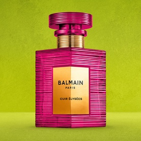 Balmain Cuir &Eacute;lys&eacute;es Eau de Parfum in a textured magenta bottle with gold cap and label, on a green background