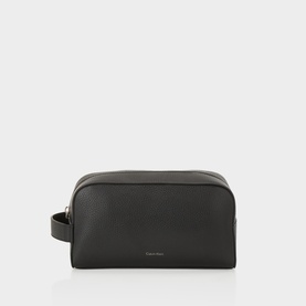 Calvin Klein Foil Logo Wash Bag in black grained leather, top zip closure, silver-tone logo lettering, side carry handle