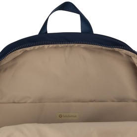 Lululemon True Navy backpack, open top view showing beige interior lining with branded logo tab.