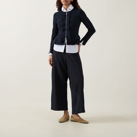 Model wearing HIGH Sapphire Pocket Jacket in navy with round neckline, peplum hem, styled with pinstripe wide-leg trousers and nude flats.