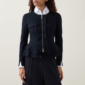 Model wearing HIGH Sapphire Pocket Jacket in navy with zip fastening, peplum hem and chest pockets, styled with pinstripe trousers.