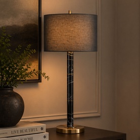 Mindy Browne Newton Table Lamp in black grey with marble column, brass base, and grey drum shade, styled on a sideboard in a living room setting.
