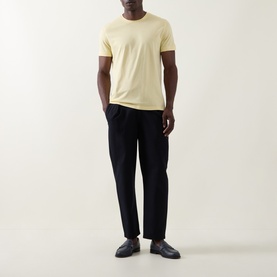Model wearing Boss Black Casual Taut Logo T-Shirt in Beige Overflow, crew neck, short sleeves, styled with black tapered trousers and dark loafers.