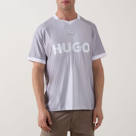 Model wearing Hugo Dwild Logo T-Shirt in light pastel green with shaped neckline, short sleeves, and bold chest logo, styled with khaki trousers
