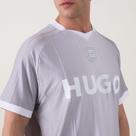 Model wearing Hugo Dwild Logo T-Shirt in light pastel green with diamond print, V-neckline, white trim, and bold HUGO chest logo.
