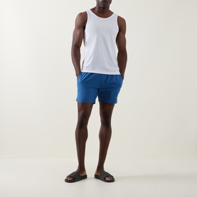 Model wearing Hugo Boss blue swim shorts with white vest top and brown leather slides.