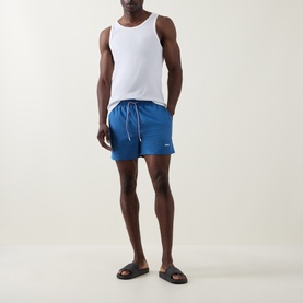 Model wearing Hugo Boss blue swim shorts with drawstring waist, styled with a white vest top and black slides.