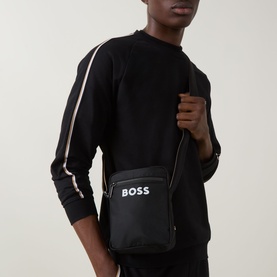 Model carrying Hugo Boss Catch 3.0 Logo Crossbody Bag in black with white contrast logo, adjustable striped strap, styled with black sweatshirt