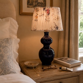 Mindy Browne Cyrus Floral Table Lamp in navy blue with cream pleated floral shade, styled on a bedside table in a bedroom setting.