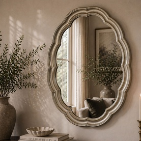 Mindy Browne Emily Framed Mirror in gold with scalloped oval frame, styled in a warm living space with botanical accents