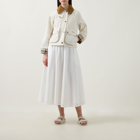 Model wearing Barbour Melody Broderie Anglaise Skirt in white, midi length flared silhouette, styled with cream quilted jacket and sandals.