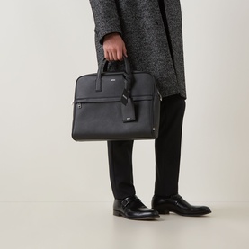 Model carrying Hugo Boss Zair S Document Briefcase in black faux leather with silver-tone hardware and top handles, styled with dark trousers and coat