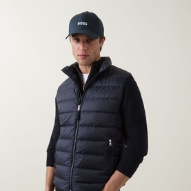 Model with Hugo Boss Zed Logo Baseball Cap in navy, styled with a navy quilted gilet and dark knitwear.
