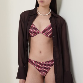Model wearing Jets rose geometric print bikini brief and triangle top, styled with an open brown shirt and pearl necklace