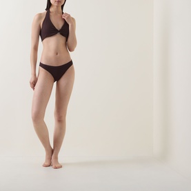 Model wearing Jets Bikini Brief in Chocolate, paired with matching halterneck bikini top. Minimal coverage, smooth nylon-elastane fabric.