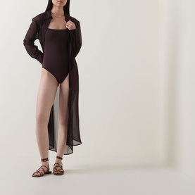 Model wearing Jets Belted Beach Shirt Dress in chocolate, sheer high-low hem, long sleeves, styled with a dark bodysuit and tan gladiator sandals