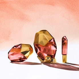 OREBELLA Eternal Roots Parfum 50ml in faceted amber and gold bottles, shown in three sizes against a soft coral watercolour background
