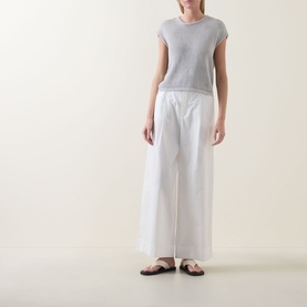 Model wearing Transit Open-Knit Sweater in light grey with round neck and cap sleeves, styled with wide-leg white trousers and black flat sandals.