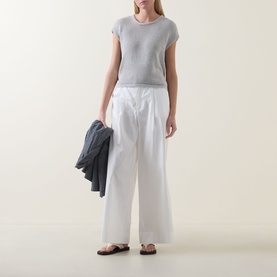 Model wearing Transit Open-Knit Sweater in Light Grey with white wide-leg trousers and black sandals, carrying a dark jacket.