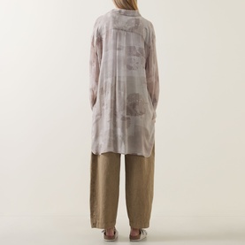 Model wearing Transit Tonal Printed Longline Shirt in sand, semi-sheer with high-low hem, styled with wide-leg taupe trousers. Rear view.