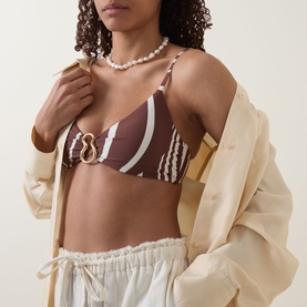 Model wearing Seafolly Coastline Ring Bralette Bikini Top in Cocoa with white stripe print and gold ring detail, styled with cream jacket and white