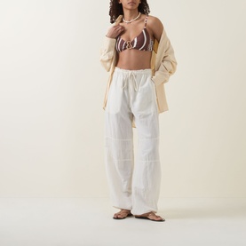 Model wearing Seafolly Coastline Ring Bralette Bikini Top in Cocoa with metallic ring detail, styled with white wide-leg trousers and an open shirt