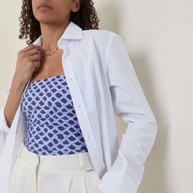 Model wearing Seafolly Marseille Bandeau Swimsuit in Blue Indigo with geometric print, styled with a white oversized shirt and white trousers.