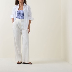 Model wearing Seafolly Marseille Bandeau Swimsuit in Blue Indigo with white linen trousers, blazer and black sandals.